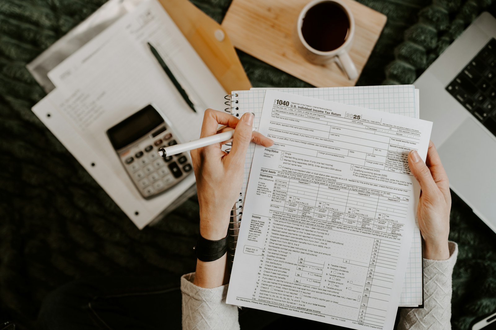 Hands working through paperwork with a calculator and laptop
